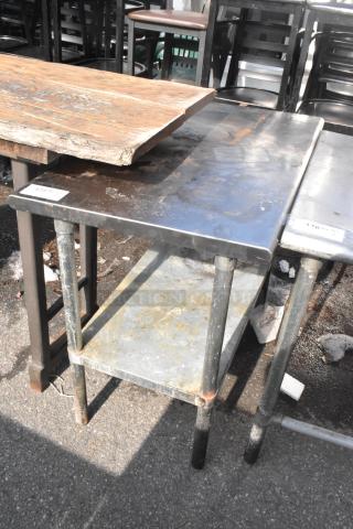 Commercial table with under shelf, metal construction, visible wear, outdoor setting, auction label attached.