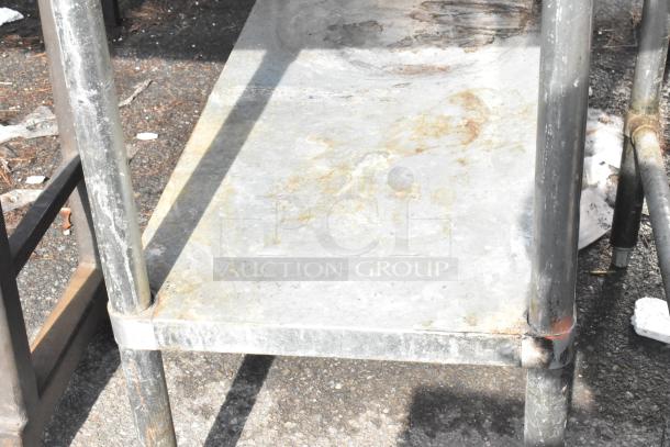 Commercial metal table with under shelf, weathered condition, showing surface rust and discoloration.