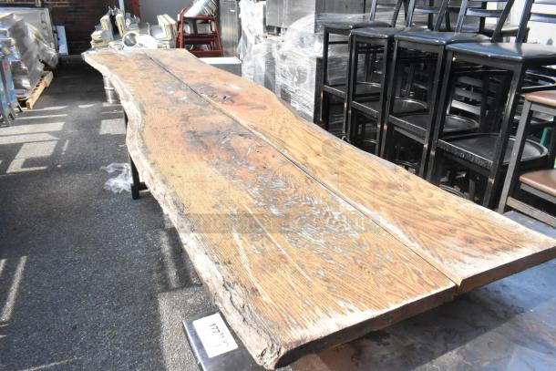 Commercial butcher block table with natural edge, rustic finish, visible wear and grain patterns, on sturdy metal legs.
