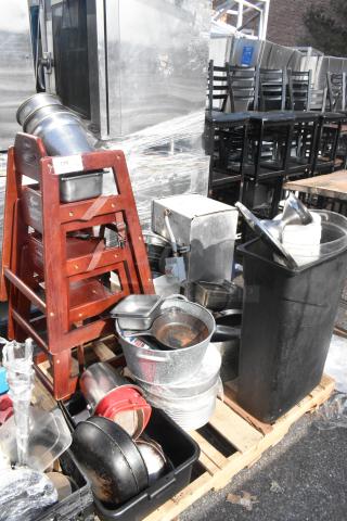 Pallet of assorted items including an evaporator, wooden high chairs, trash can, and various skillets, stacked for auction.