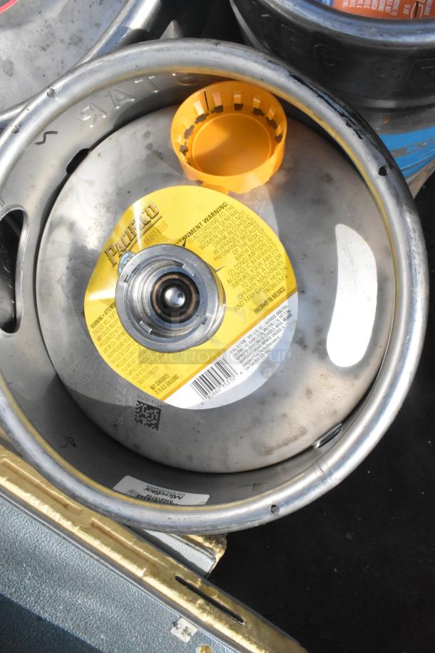 12 assorted kegs, prominently featuring a Pacifico keg with a yellow label, in used condition.