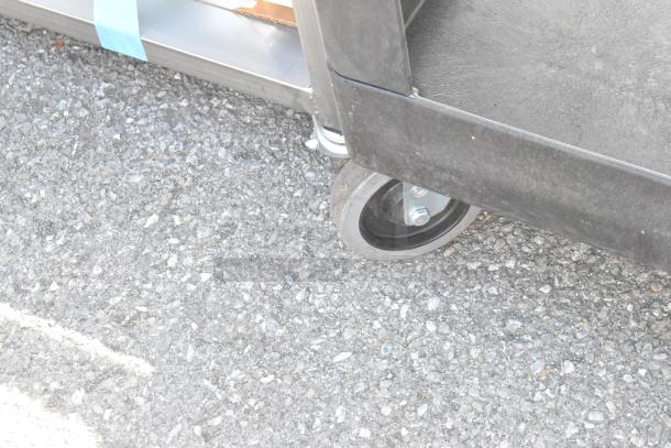 Rubbermaid Brute Poly 2 Tier Cart showing commercial caster on asphalt.
