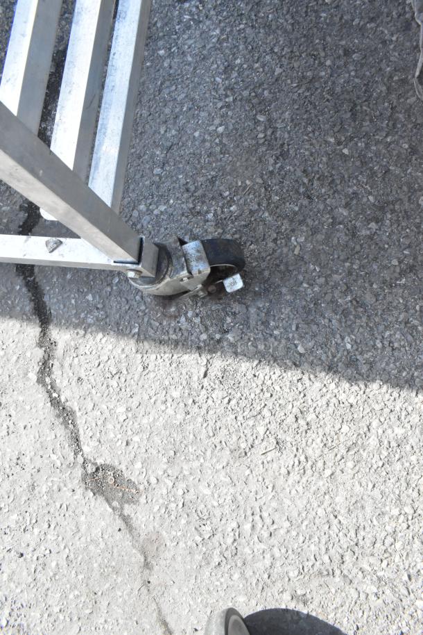 Commercial pan transport rack with sturdy frame and commercial casters, shown on asphalt. Visible wear on casters.