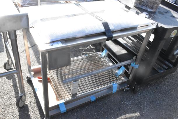 Stainless steel table on commercial casters, two-tier design, includes grate shelf. Condition: Used. Auction tag: Lot 192.