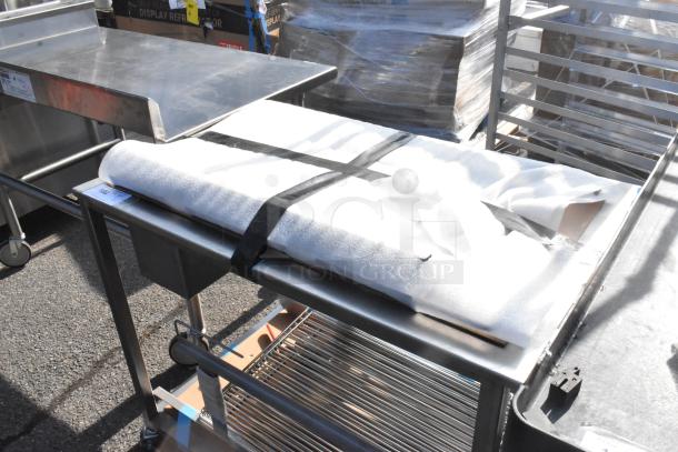 Stainless steel table on commercial casters with a flat top, lower shelf, and wrapped sheet on top. Equipped with wheels for mobility.