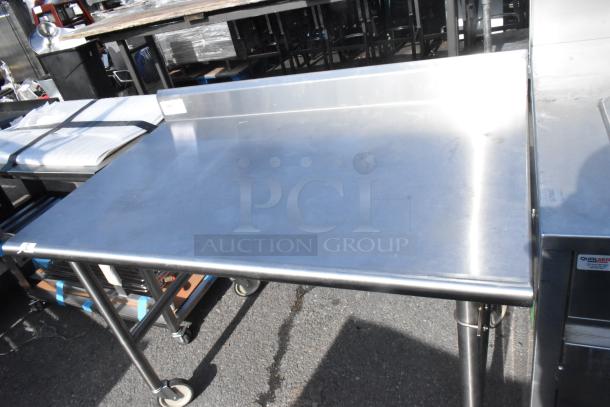 Stainless steel table with commercial casters, featuring a raised edge. In good condition, ideal for commercial use.