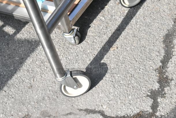 Steel table with sturdy commercial casters, shown on asphalt. Features a durable metal frame, ideal for industrial use.