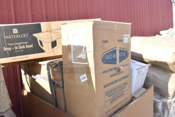 Boxes of new scratch and dent items, including Bobrick dispenser and Waterloo sink bowl, visible signs of damage.