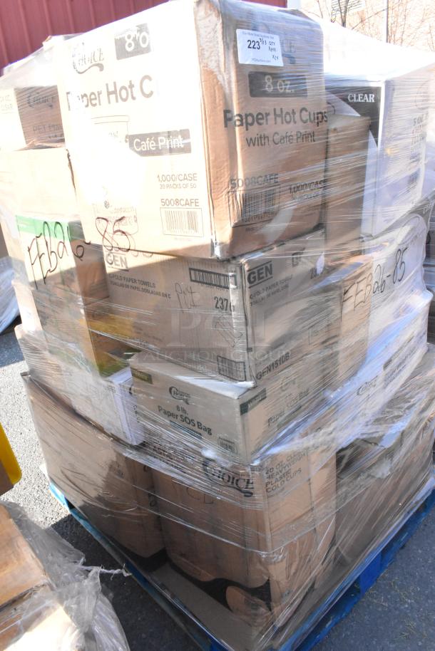 A pallet stacked with various boxed items including paper hot cups, lids, plates, and bags, some labeled as scratch and dent.