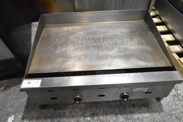 Commercial countertop gas griddle, flat top, stainless steel, visible wear on surface, dual control knobs, auction tag present.