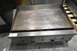 Commercial countertop gas griddle, flat top, stainless steel, visible wear on surface, dual control knobs, auction tag present.