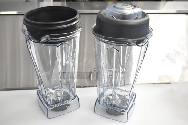 Two brand new clear poly blender pitchers, scratch and dent condition, with black lids and measurement markings.