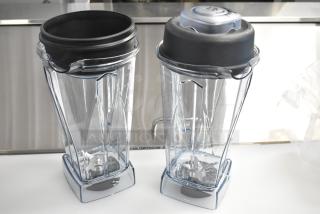 Two brand new clear poly blender pitchers, scratch and dent condition, with black lids and measurement markings.