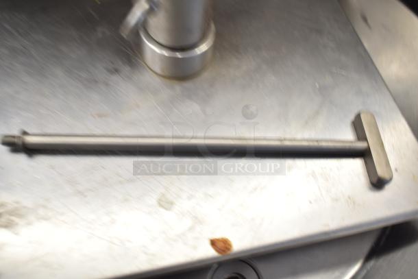 Blurry image of a metallic rod on a stainless steel surface, possibly a component of the described Inoksan machine.