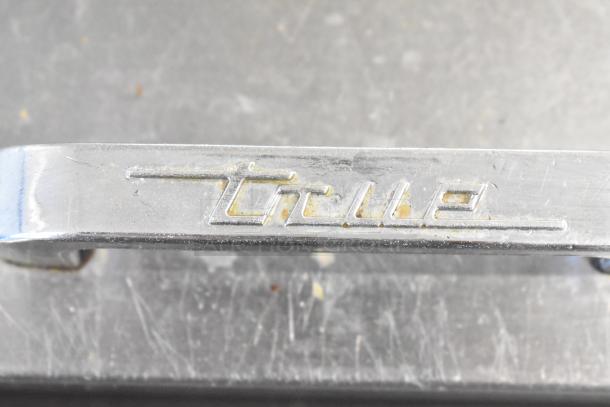 Close-up of a True TSSU-48-12 Commercial Sandwich Prep Table handle, showing the brand logo etched on metal.