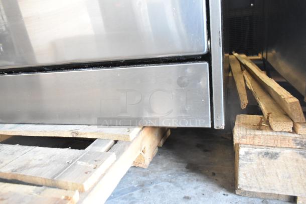 Garland SunFire commercial gas range lower panel close-up. Stainless steel surface with minor wear. Resting on wooden pallets.