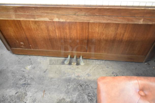 Baldwin piano with three pedals, showing wood grain finish and slight wear, accompanied by a tufted piano bench.