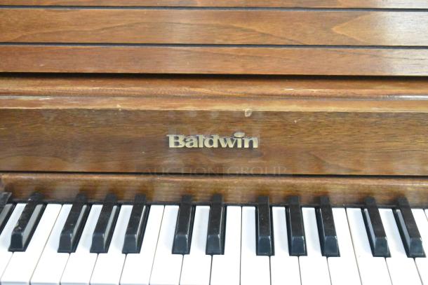 Baldwin upright piano with bench, wooden finish, visible brand logo, in used condition, showcasing keys and wood grain.