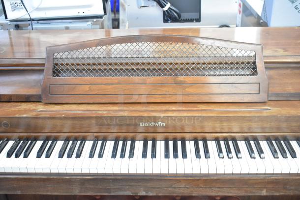 Baldwin upright piano with wooden finish and integrated music rack, includes matching piano bench; visible Baldwin logo.