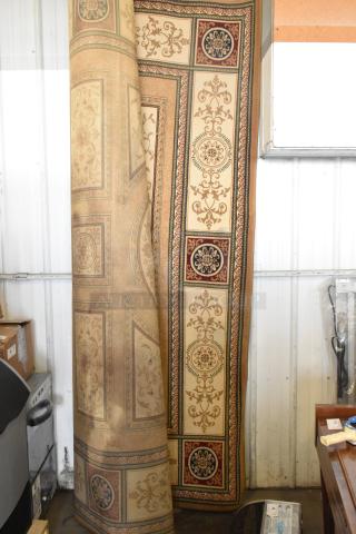 Ornate beige and burgundy rug with floral patterns, rolled partially, in good condition, suitable for auction display.