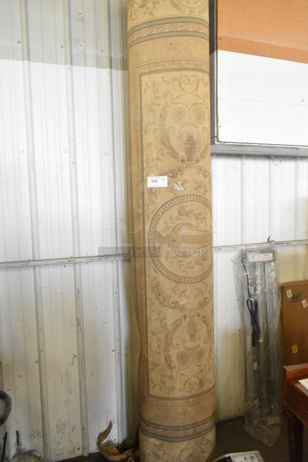 Rolled beige rug with intricate floral and urn patterns, in good condition. Auction tag labeled "112".