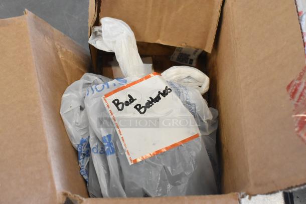 Cardboard box containing a Zebra unit and three batteries in plastic bags. Visible label reads "Bad Batteries."