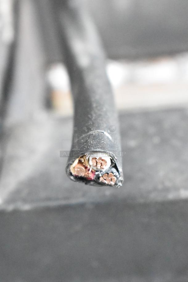 Close-up of a cut electrical cable with exposed copper wires, surrounded by a black rubber sheath, possibly for industrial use.