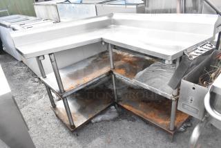 Commercial L-shaped table with two metal under shelves, visible rust, sturdy metal structure, suitable for industrial use.