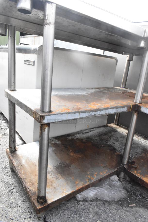 Commercial L-shaped table with two metal under shelves, showing visible rust and wear, sturdy metal construction.
