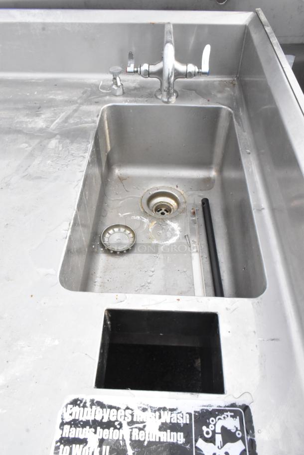 Commercial single bay stainless steel sink with faucet and under shelf, used condition. Features safety sign and visible wear.