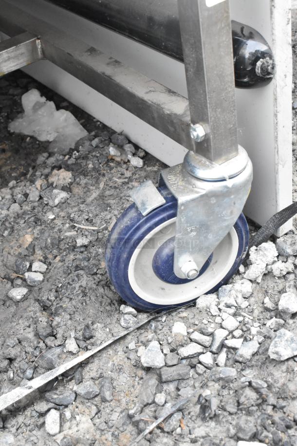 Commercial table on blue casters, showing sturdy construction. Ideal for mobility, includes drawer and under shelf. Good condition.
