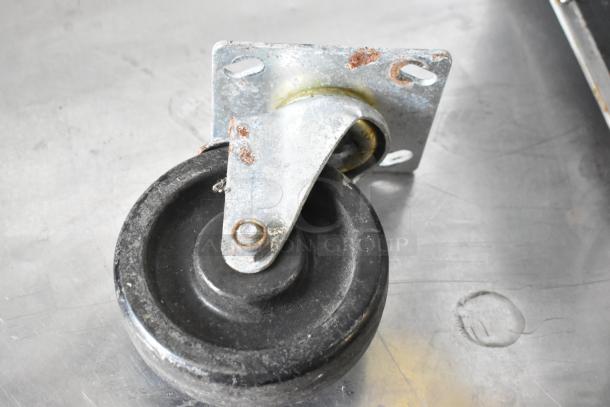 Lot of 4 commercial casters, metal brackets with black rubber wheels, used condition with visible rust on brackets.