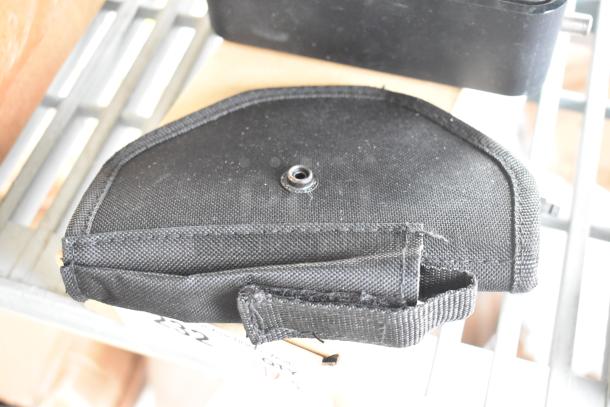 Five various items including a black fabric pouch with a snap button, stored on a metal shelf.