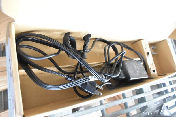 Box containing a power adapter with attached cable and plug, secured with a velcro strap. Suitable for various electronic devices.