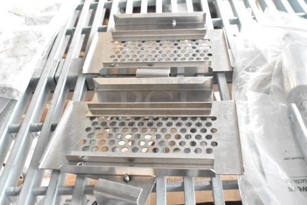 Nine metal components on a pallet, includes perforated and non-perforated pieces. Condition appears new with packaging. No visible labels.
