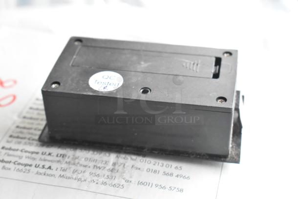 Black electronic device with a "QC Tested" sticker, part of a lot including Accucold Alarm and Robot Coupe blade.