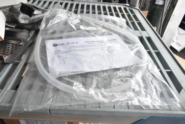 Nine various items including Bunn hose, Accucold alarm, stickers, Robot Coupe blade, and more. New, in packaging.