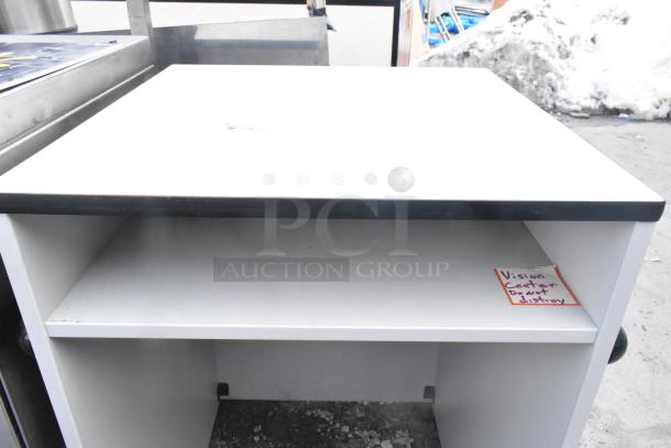 White counter with black trim, featuring a shelf. Visible label reads "Vision Center Do not destroy." Slight wear on surfaces.