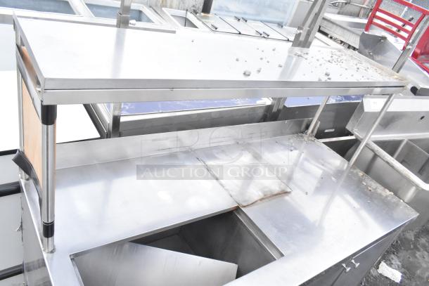 Commercial stainless steel counter with cut out, over shelf, and three doors, showing signs of wear.