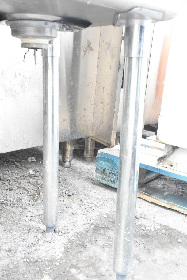 Commercial 3 bay sink with right side drain board, featuring sturdy metal legs, visible under-sink plumbing, and signs of wear.