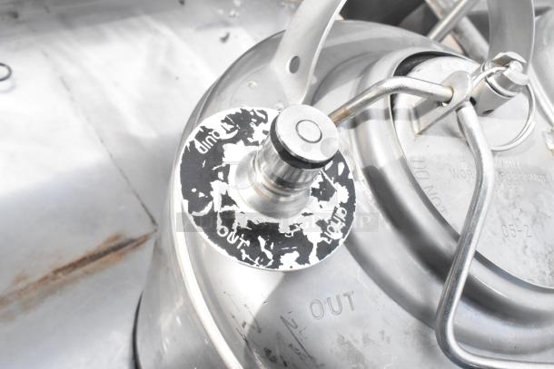 Two metal 3-gallon kegs with sturdy handles and labeled "in" and "out" for liquid flow control. Visible wear.