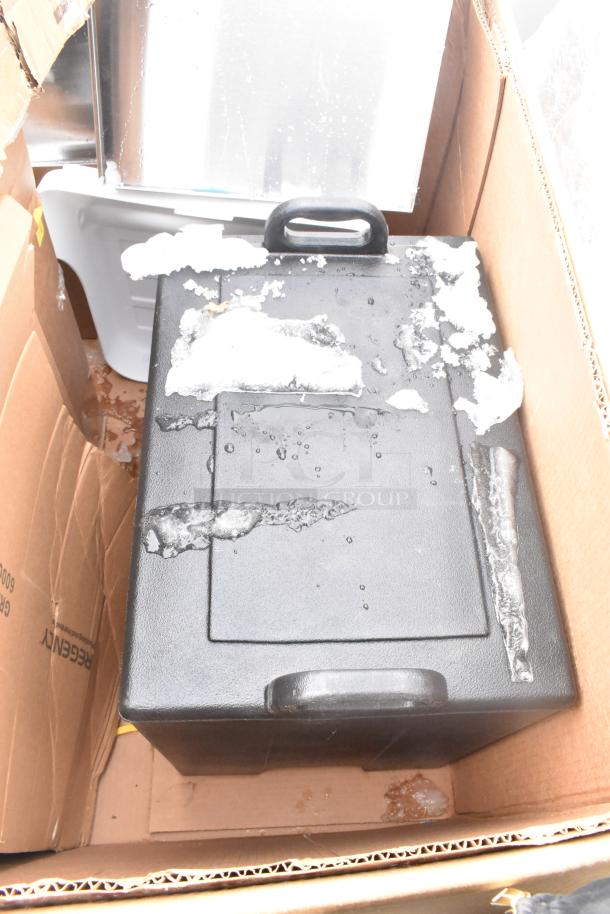 Black Cambro front load catering case, new with scratches and dents, in cardboard box, partially covered with ice.