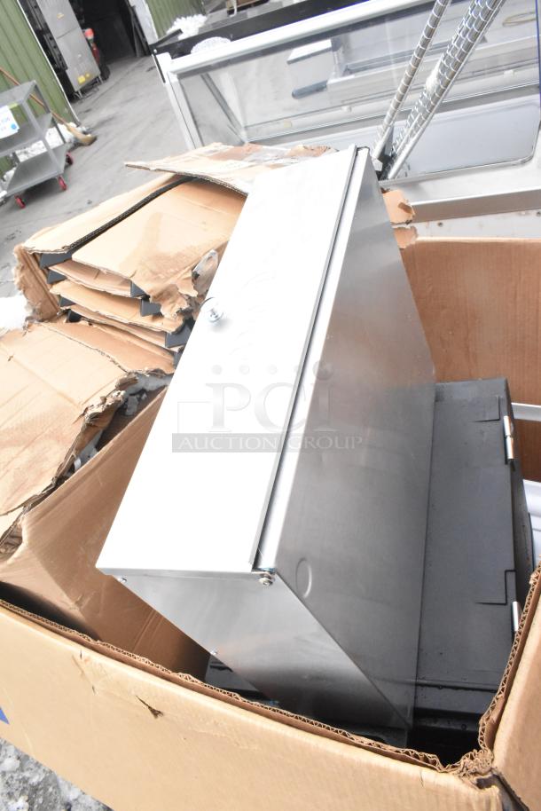 Cardboard box with new items including a Cambro front load catering case and trays. Box shows minor damage; items inside appear untouched.