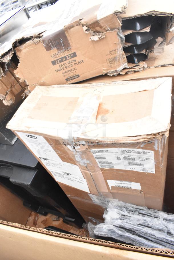 Cardboard boxes containing scratch and dent items, including Cambro catering case. Labels show "Lancaster Table & Seating" and "22 x 22 Cast Iron Table Base Plate." Boxes are worn.