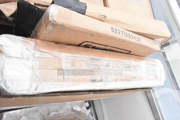 Stack of new, scratched, dented items in boxes labeled "Regency" and "Steelton," including trays and bussing carts.