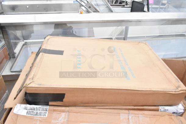Cardboard box labeled "FRAGILE," containing new scratch and dent trays, on a metal countertop. Box markings suggest delicate glass items.