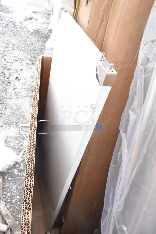 Alt text: Scratch and dent item, likely a table panel, leaning against cardboard packaging. Visible wear on metal corners.