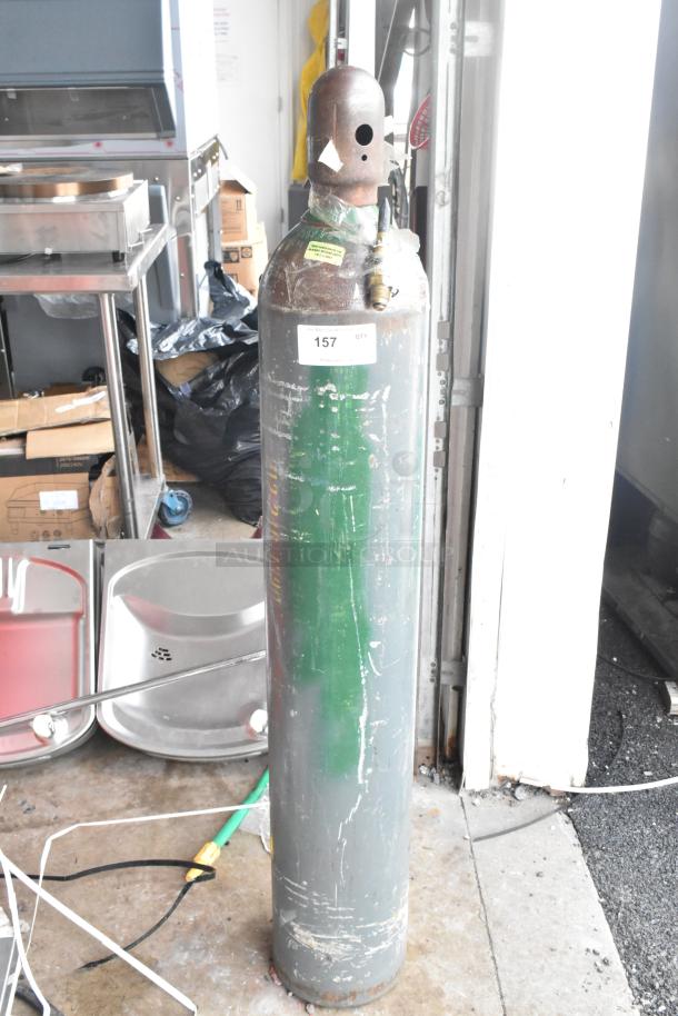 Metal cylinder tank with attached valve, tagged "157". Scratched, weathered exterior. Buyer must pick up; no shipping available.