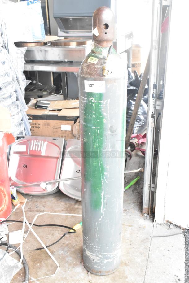 Industrial tank with metal body, number 157 label, requires pickup. Visible signs of wear, suitable for industrial use.