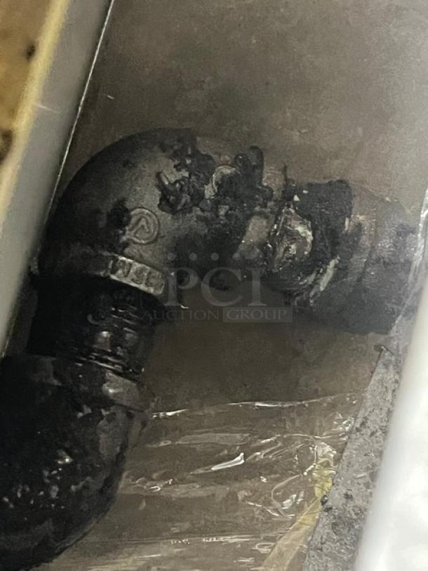 Stainless steel elbow pipe fitting, possibly related to gas connection for commercial char broiler. Signs of use visible.